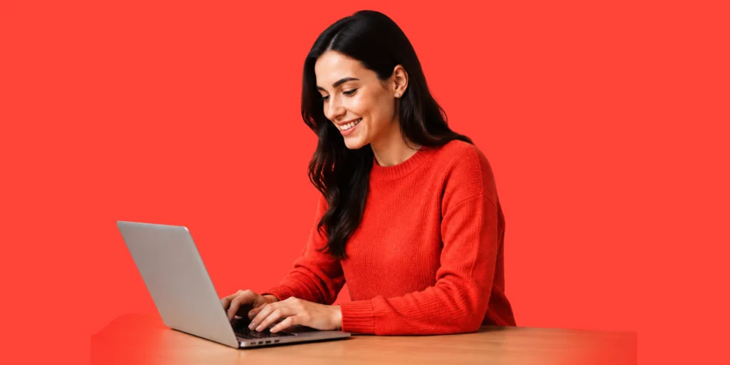 A smiling woman working on a laptop, representing our professional social media management services. Contact us to grow!